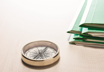 Ein Kompass und grüne Hefter auf einem Schreibtisch