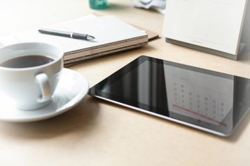 Eine volle Tasse Kaffe neben einem Tablet und einem Block auf einem Schreibtisch